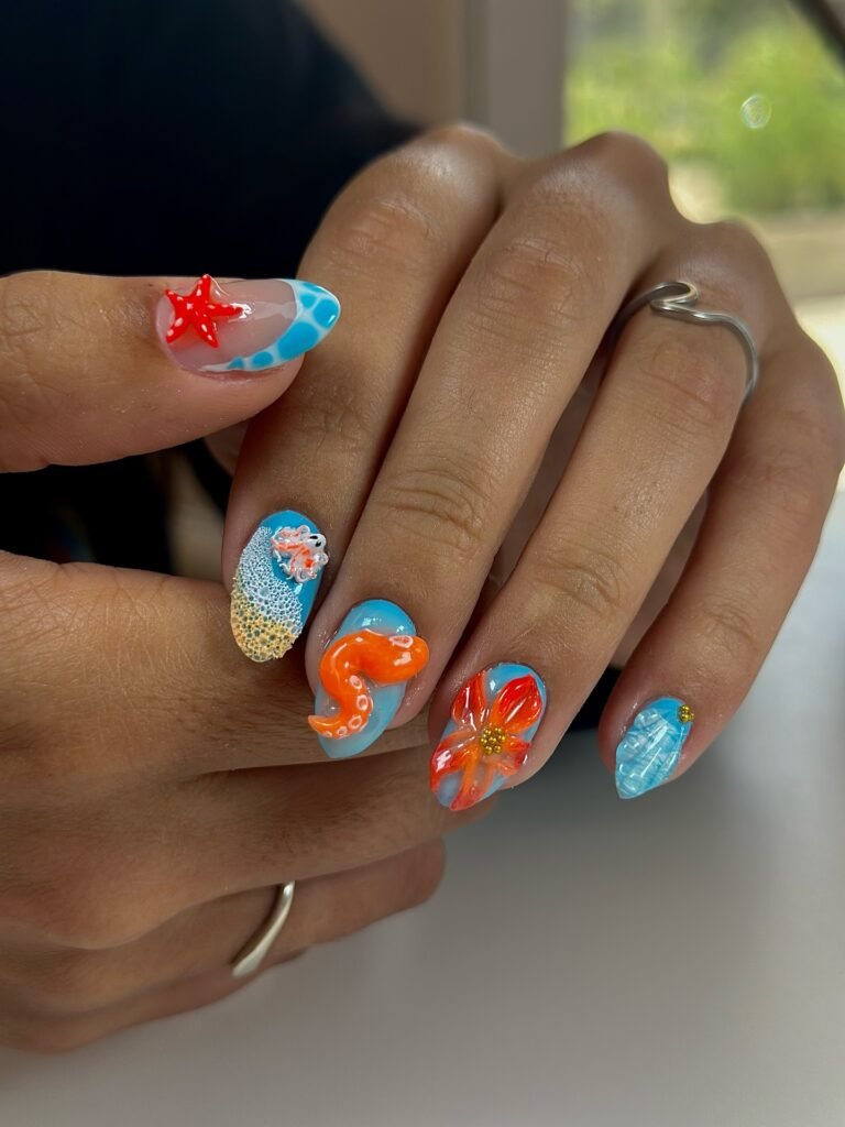 Colorful ocean-themed nail art with starfish, octopus, and floral designs. Bright, artistic manicure on hands.