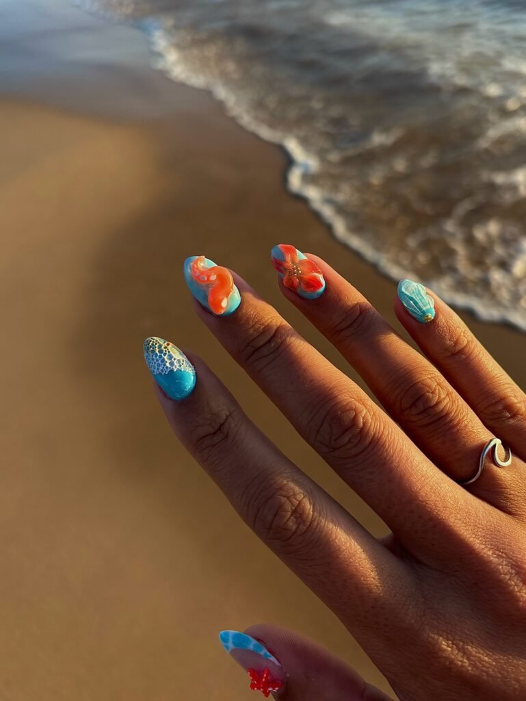Colorful beach-themed nail art with ocean and starfish design, set against a sandy shoreline background.