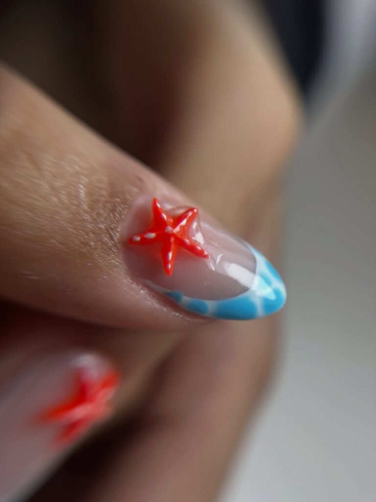 Close-up of vibrant nail art featuring a bright red star design with a blue wave detail on a clear nail.