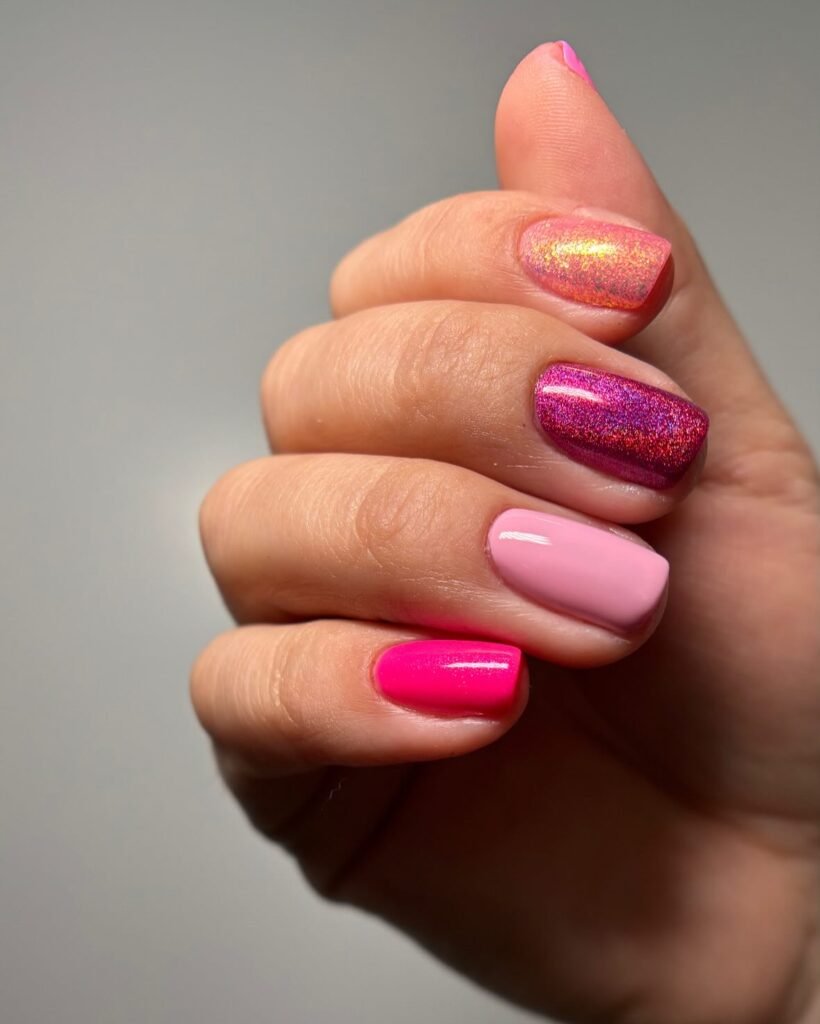Close-up of a hand with vibrant pink and glitter nail polish, showcasing a stylish, colorful manicure.