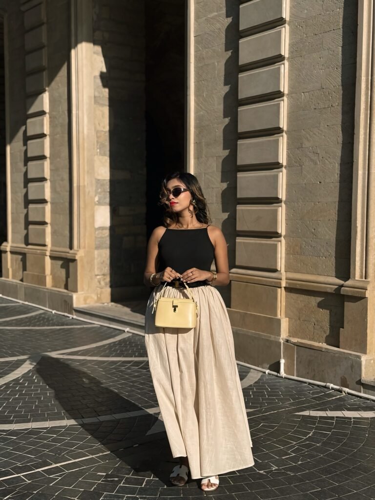 Stylish woman in chic outfit with sunglasses and yellow handbag, walking in sunny cityscape.