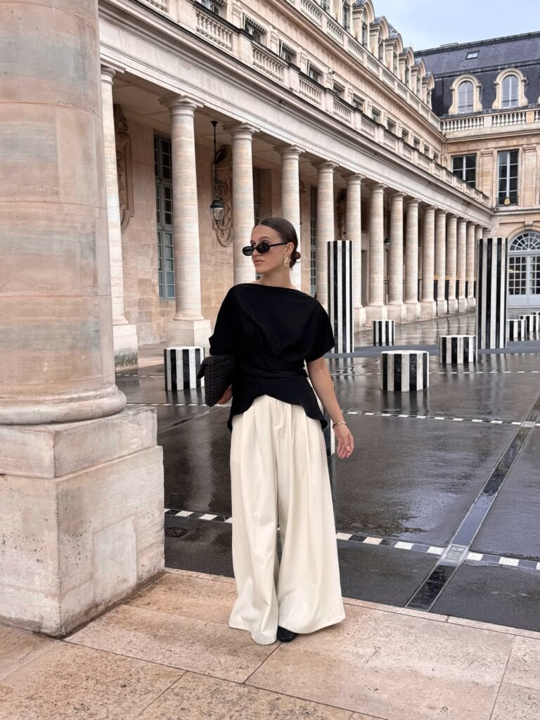 Elegant woman in chic outfit standing outside historic building with columns on a rainy day.