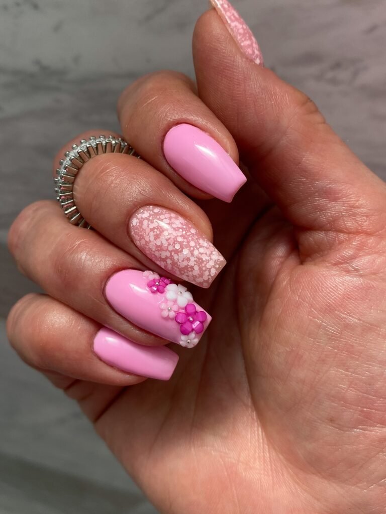 Pink manicure with floral nail art and confetti designs on medium-length nails.