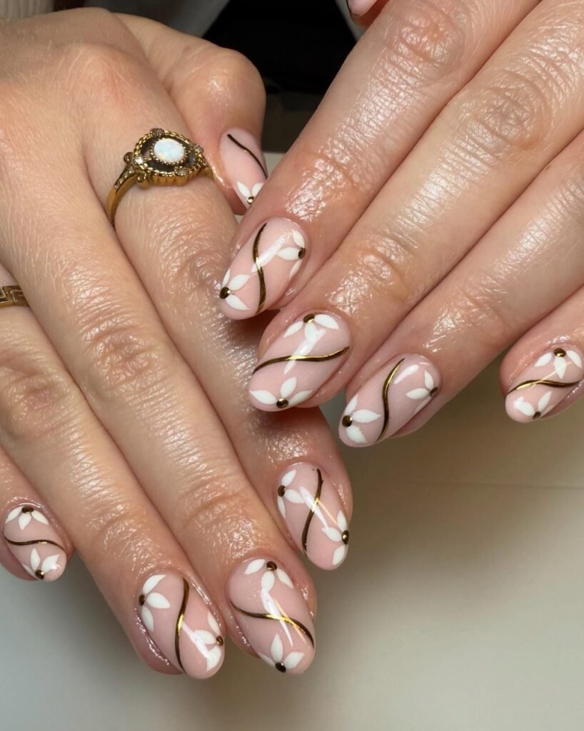 Elegant pink nail art with white floral designs and gold accents, perfect for a stylish manicure look.
