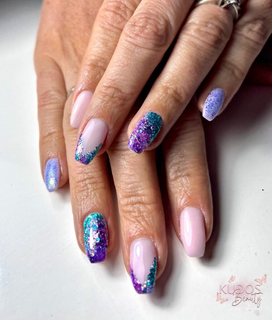 Colorful glitter nail art with purple and teal accents on manicured fingers. Trendy and stylish nail design close-up.