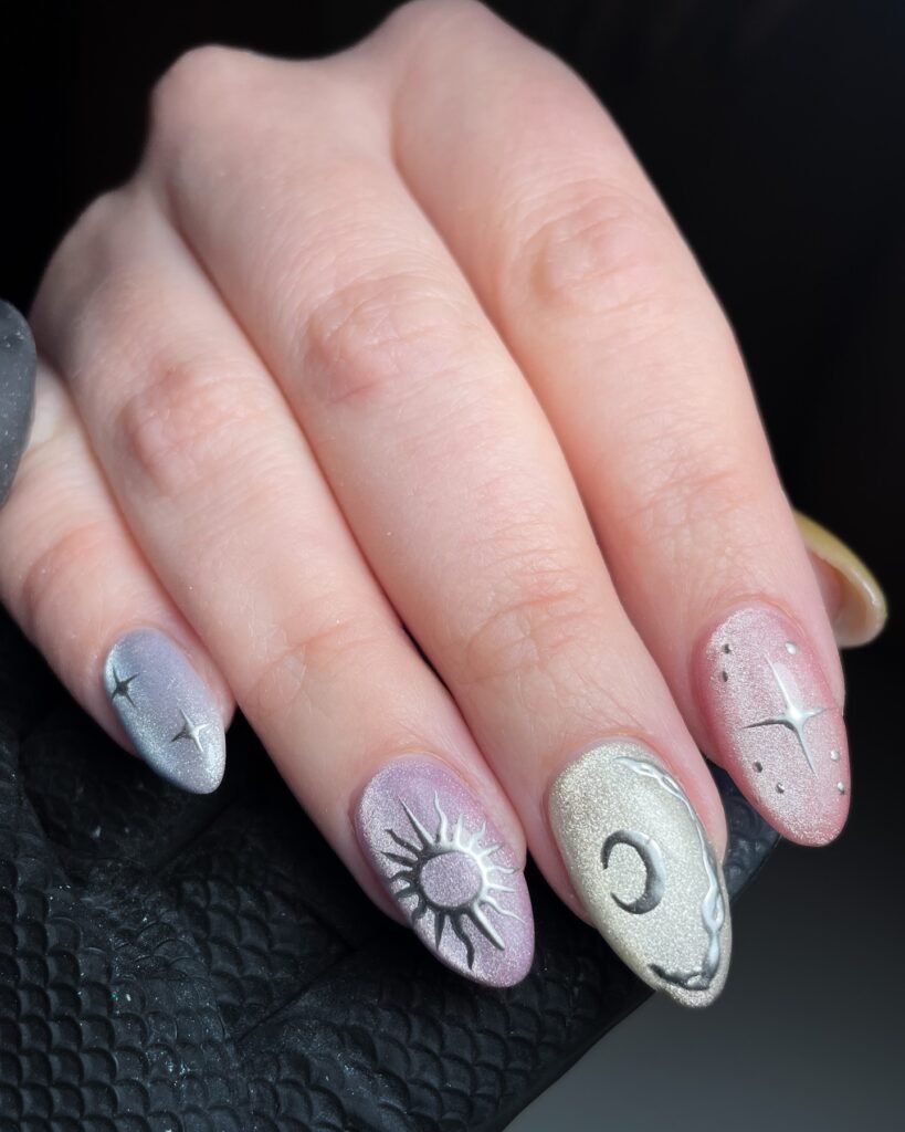 Celestial nail art with sun and moon designs on pastel shades, close-up of manicured hand.