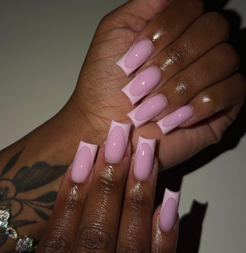 Stylish pink coffin-shaped acrylic nails with glossy finish and hand tattoo.