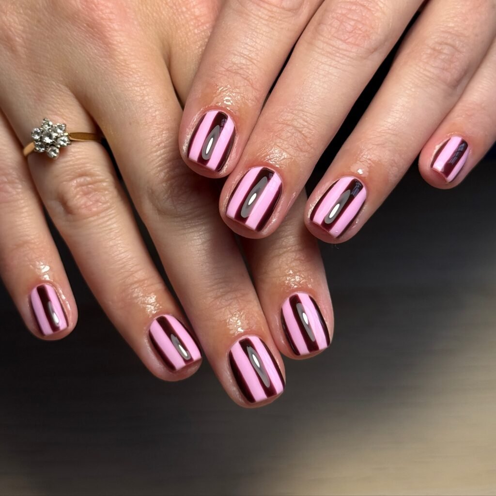 Pink and black striped nail art with glossy finish on short nails, adorned with a flower ring on one finger.