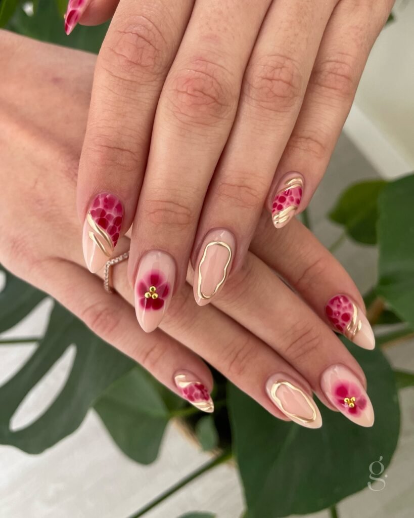 Elegant hand with pink floral nail art and subtle gold accents over green leaves background.