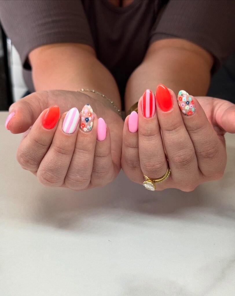 Colorful floral and striped nail art on manicured hands with gold ring.