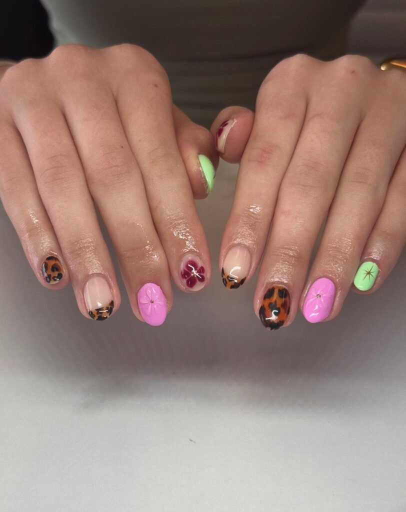 Colorful nail art showcasing floral designs and leopard print on manicured hands. Trendy and vibrant nail fashion.