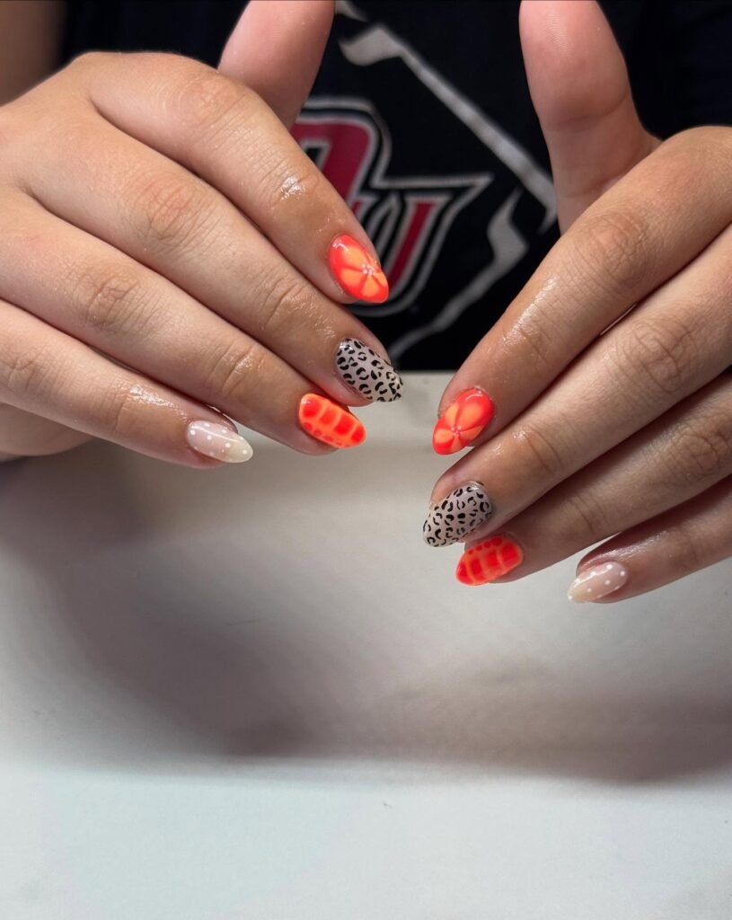 Colorful nail art with neon orange, leopard print, and polka dot designs on manicured nails.