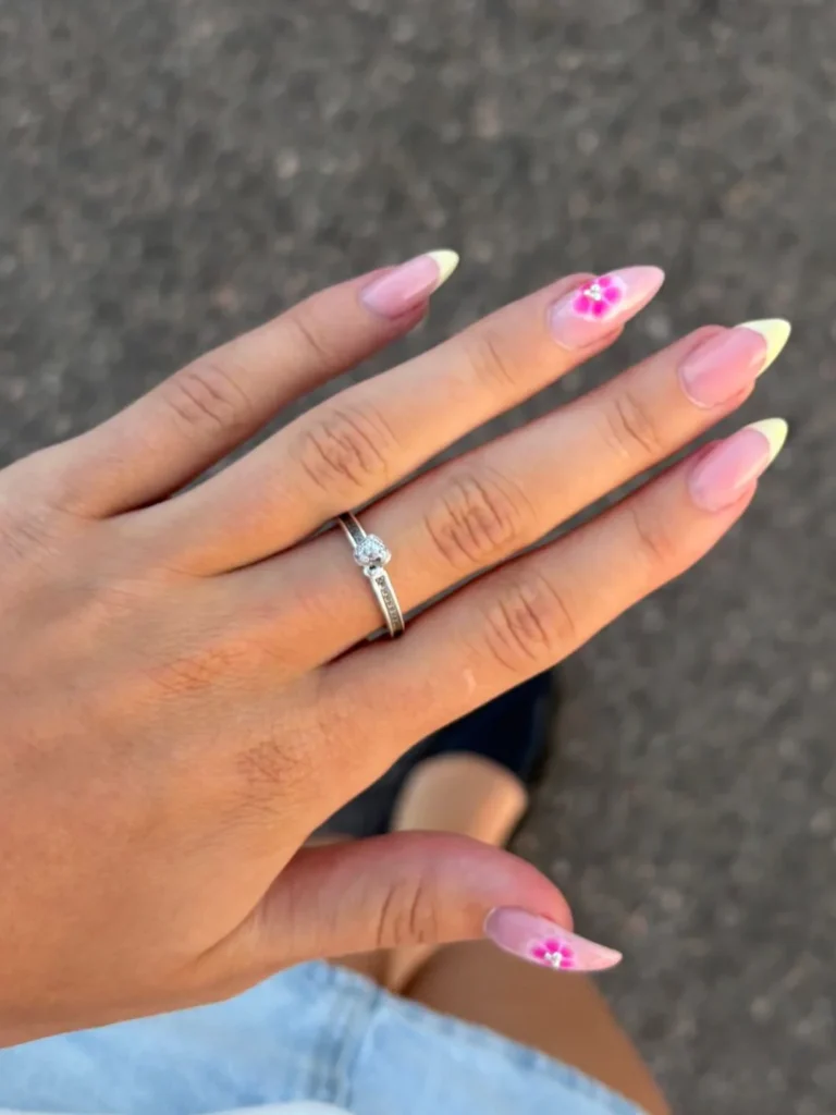 Hand with pink floral nail art and diamond ring, close-up.