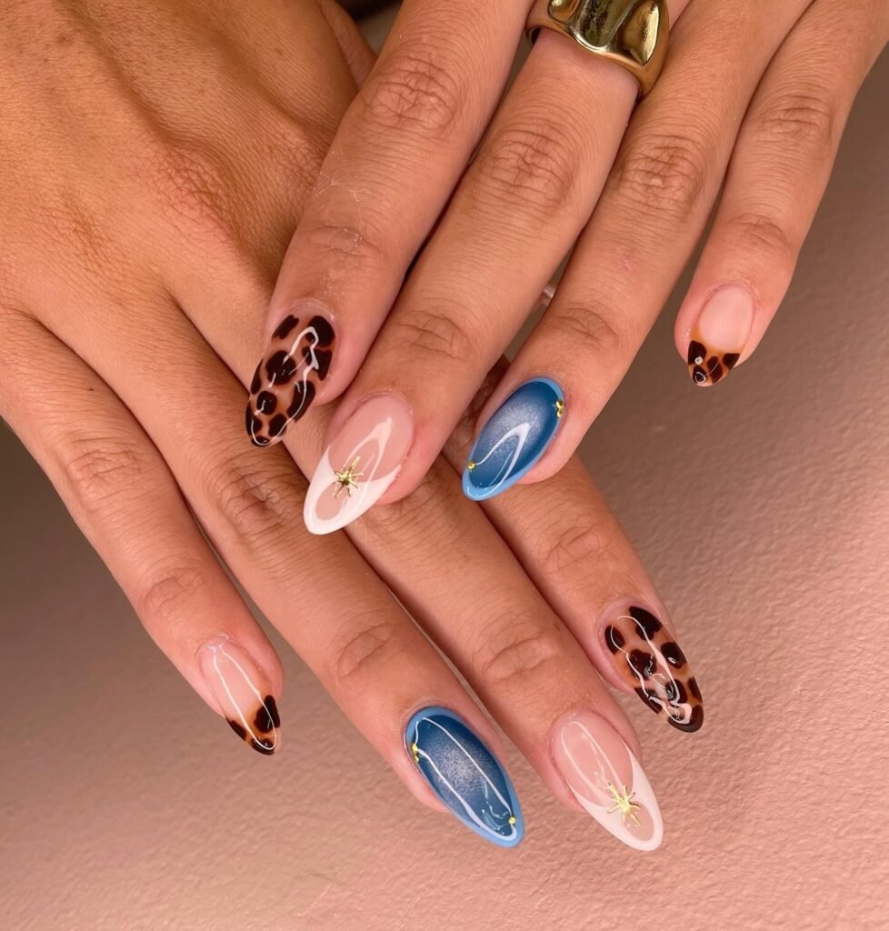 Stylish manicure with leopard, blue, and pink nail art on oval-shaped nails against a light background.