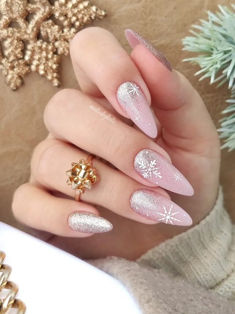 Festive stiletto nails with glitter and snowflake designs, adorned with a golden bow ring on a cozy beige background.