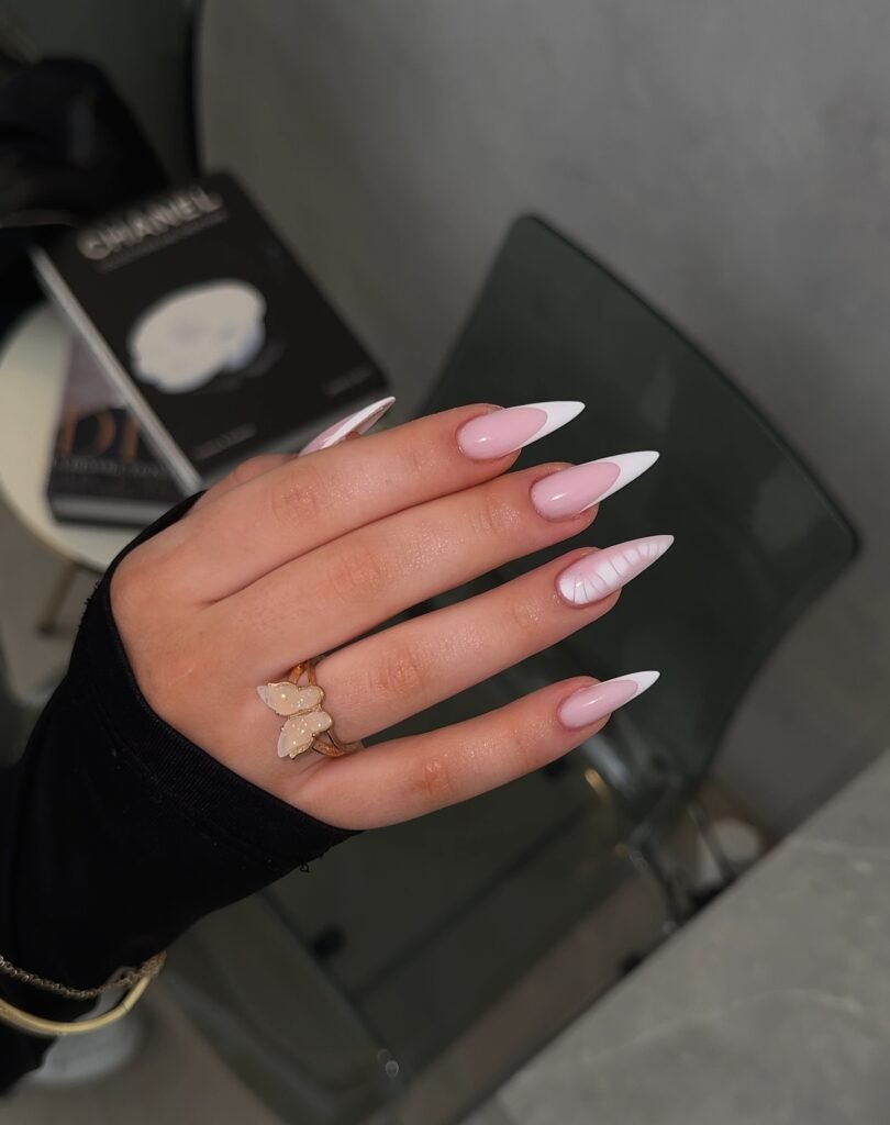 Stylish pink and white stiletto nails with a butterfly ring, featuring a unique textured design on one finger.