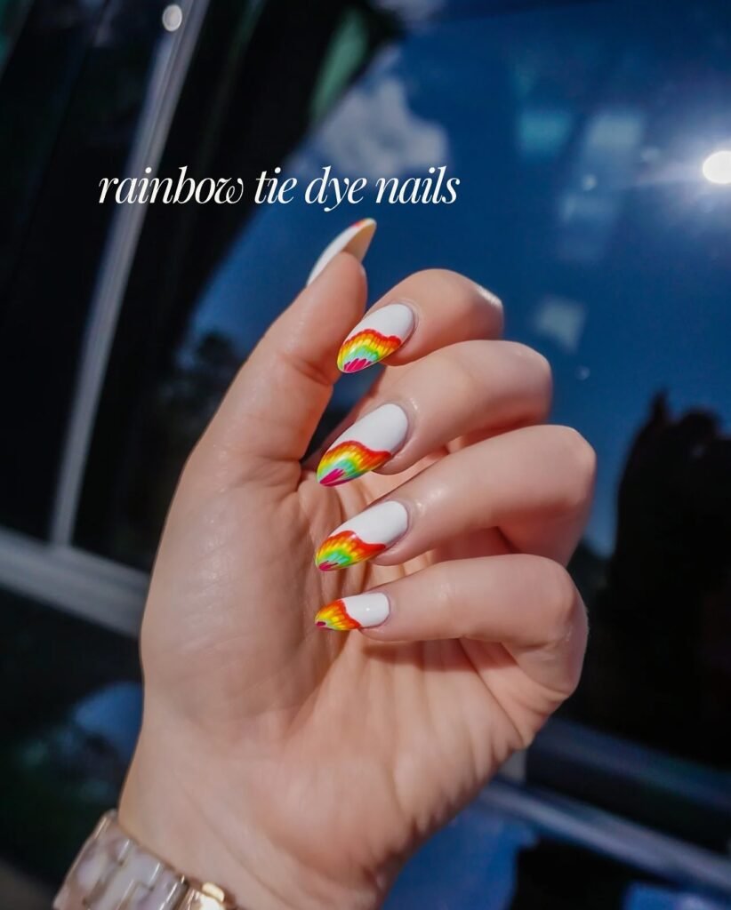 Hand with rainbow tie-dye nail art against a blue sky backdrop.