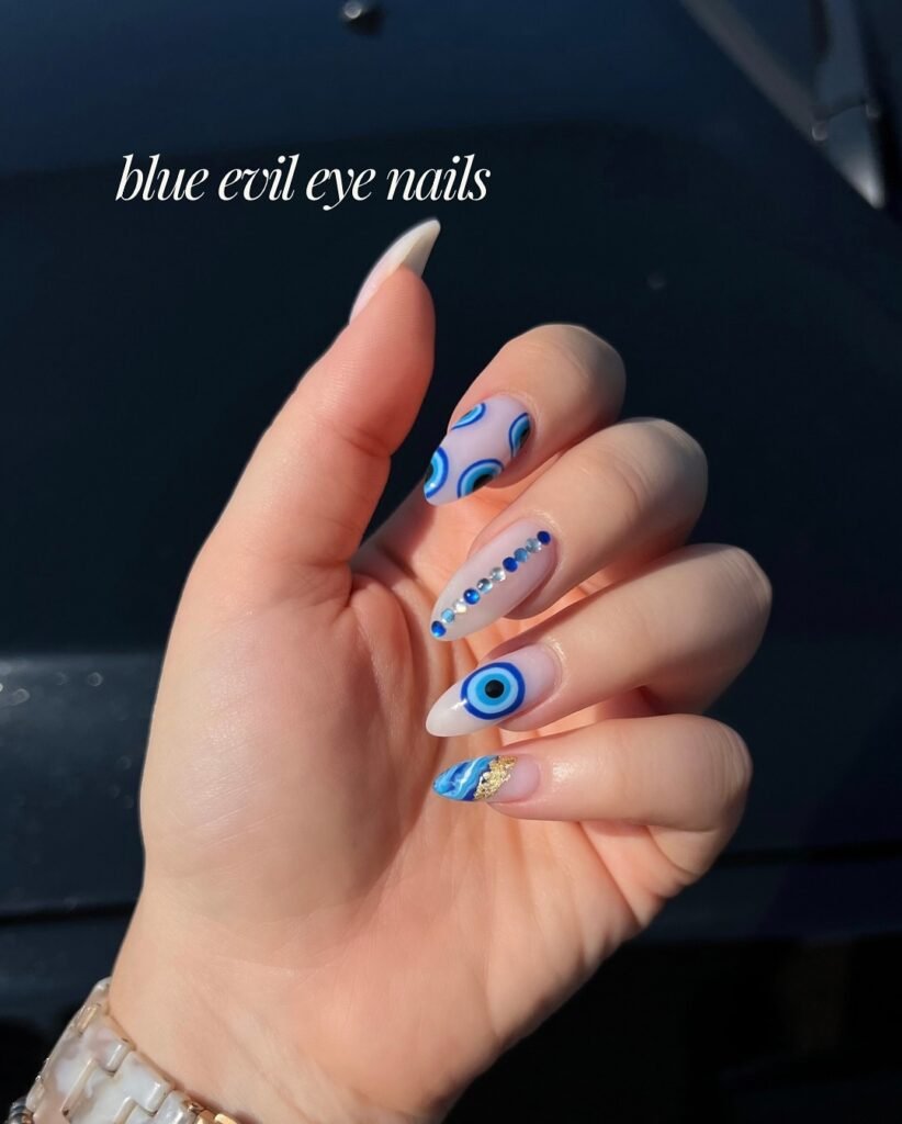 Hand with blue evil eye nail design featuring intricate patterns and gems, sunlight accentuating the details.