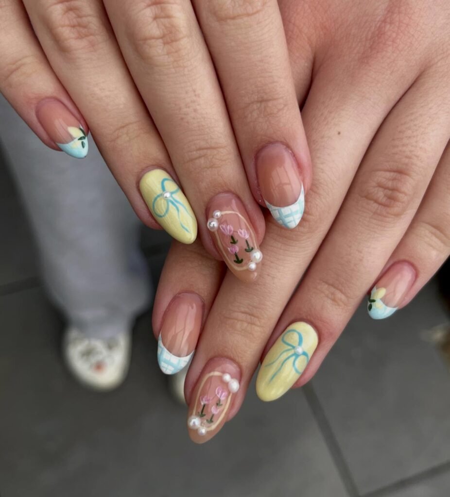 Colorful floral nail art with pearls, featuring yellow, blue, and white designs on manicured hands.