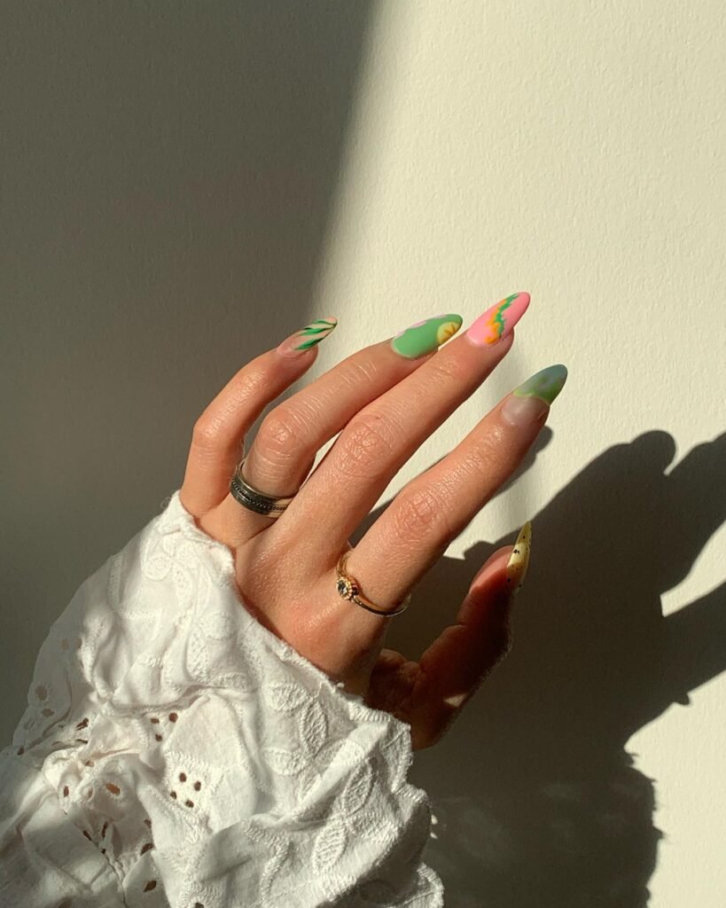 Colorful nail art on hand with rings and lacy sleeve, casting shadow on white wall.