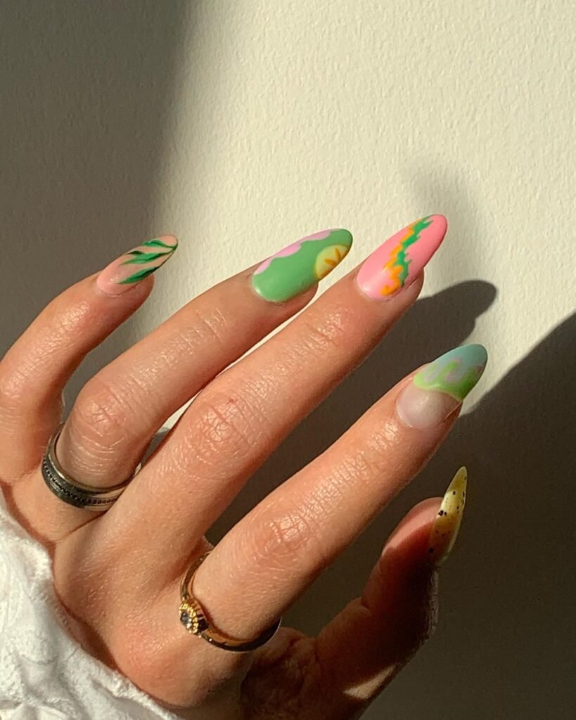 Close-up of a hand with colorful, abstract nail art in sunlight, wearing silver and gold rings.