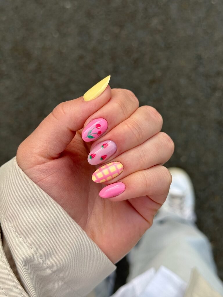 Colorful spring nails with strawberry and checkered patterns on a hand wearing a light jacket.