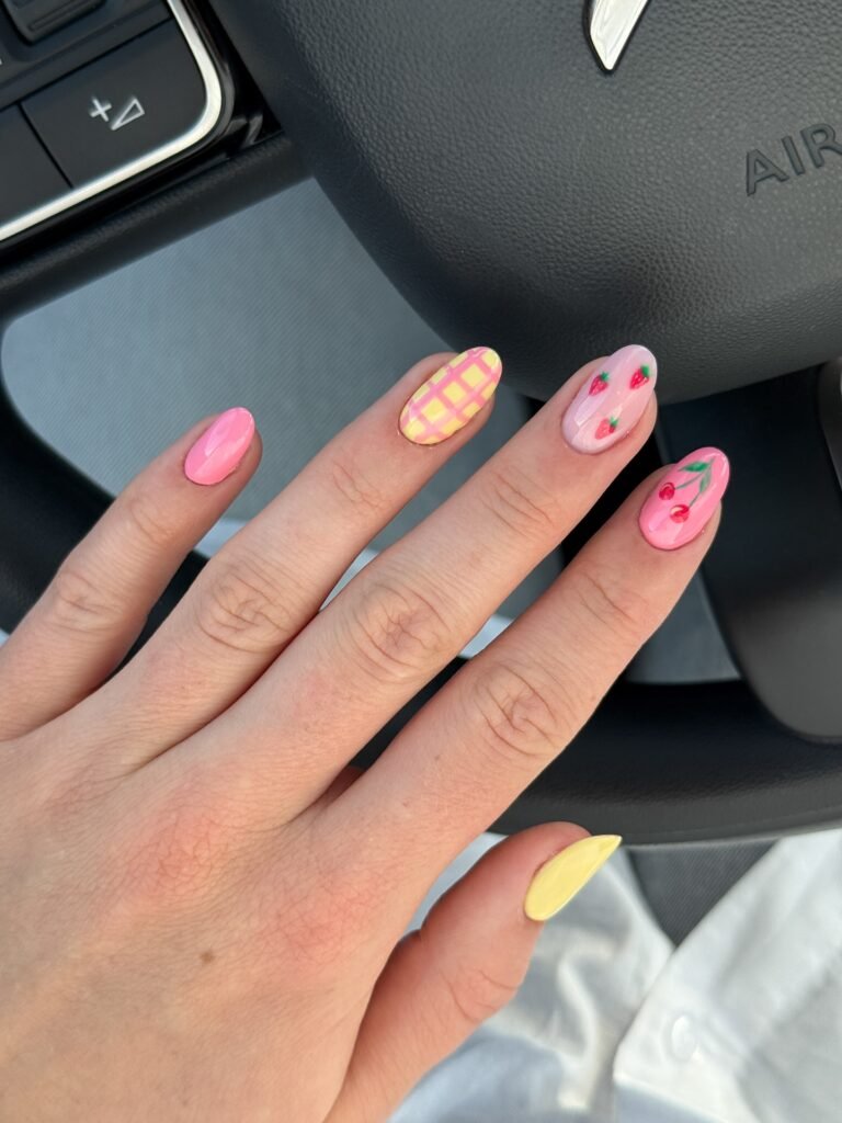 Colorful nail art with fruit designs and patterns showcased on a hand resting on a car steering wheel.