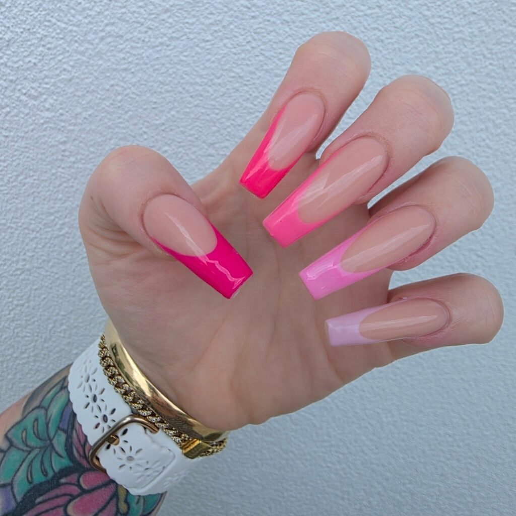 Gradient pink coffin nails with a stylish ombre design and a white bracelet on a tattooed wrist.