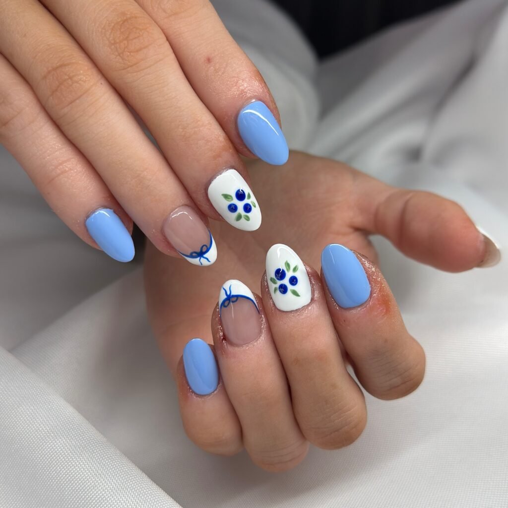 Blue and white floral nail art design on manicured hands over white fabric background.