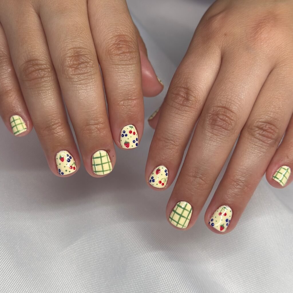 Colorful nail art with grid and berry patterns on short nails.