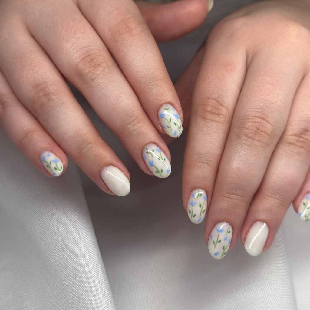 Hands with delicate white nail polish and blue flower designs on a soft fabric background.