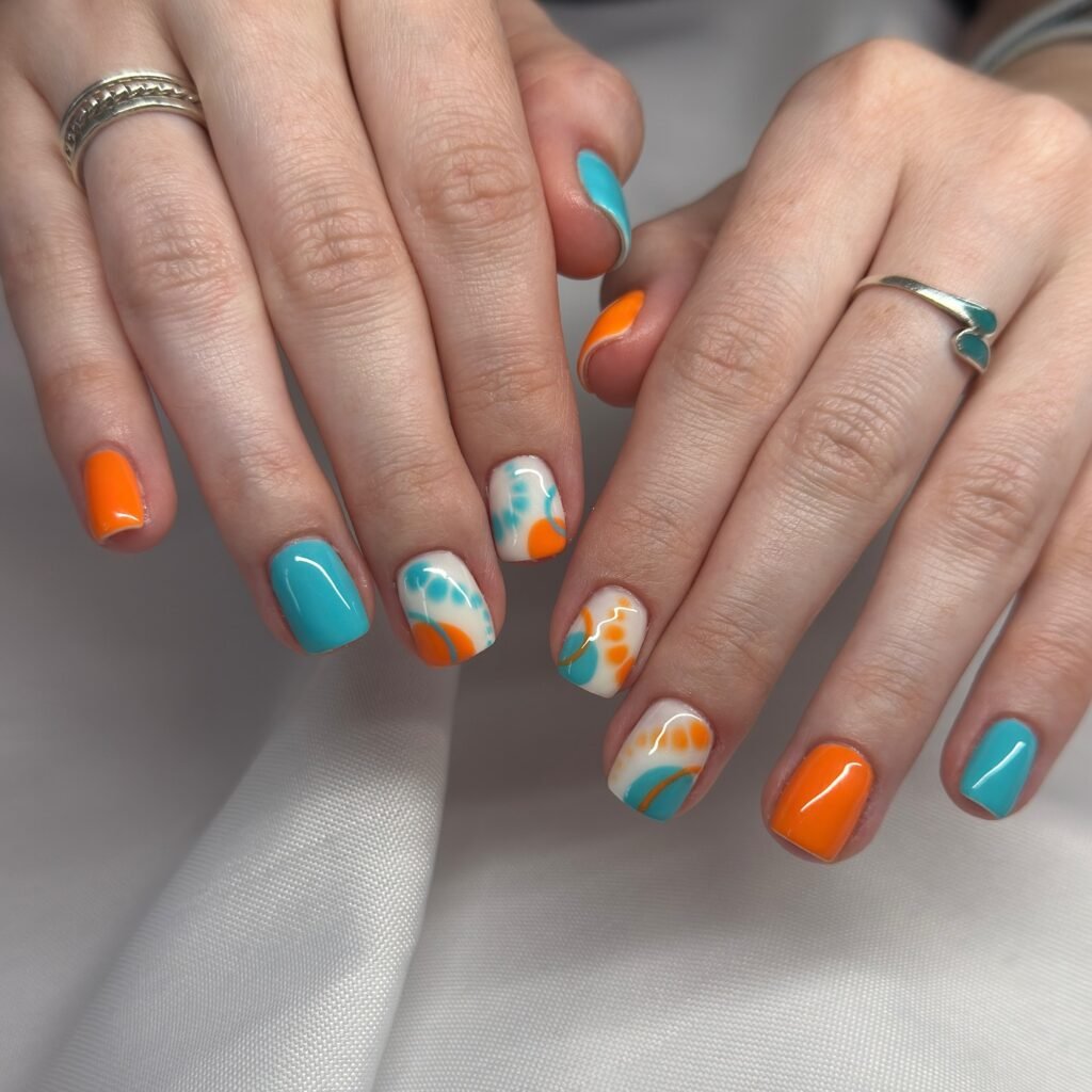 Colorful abstract nail art with turquoise and orange designs on short, manicured nails.