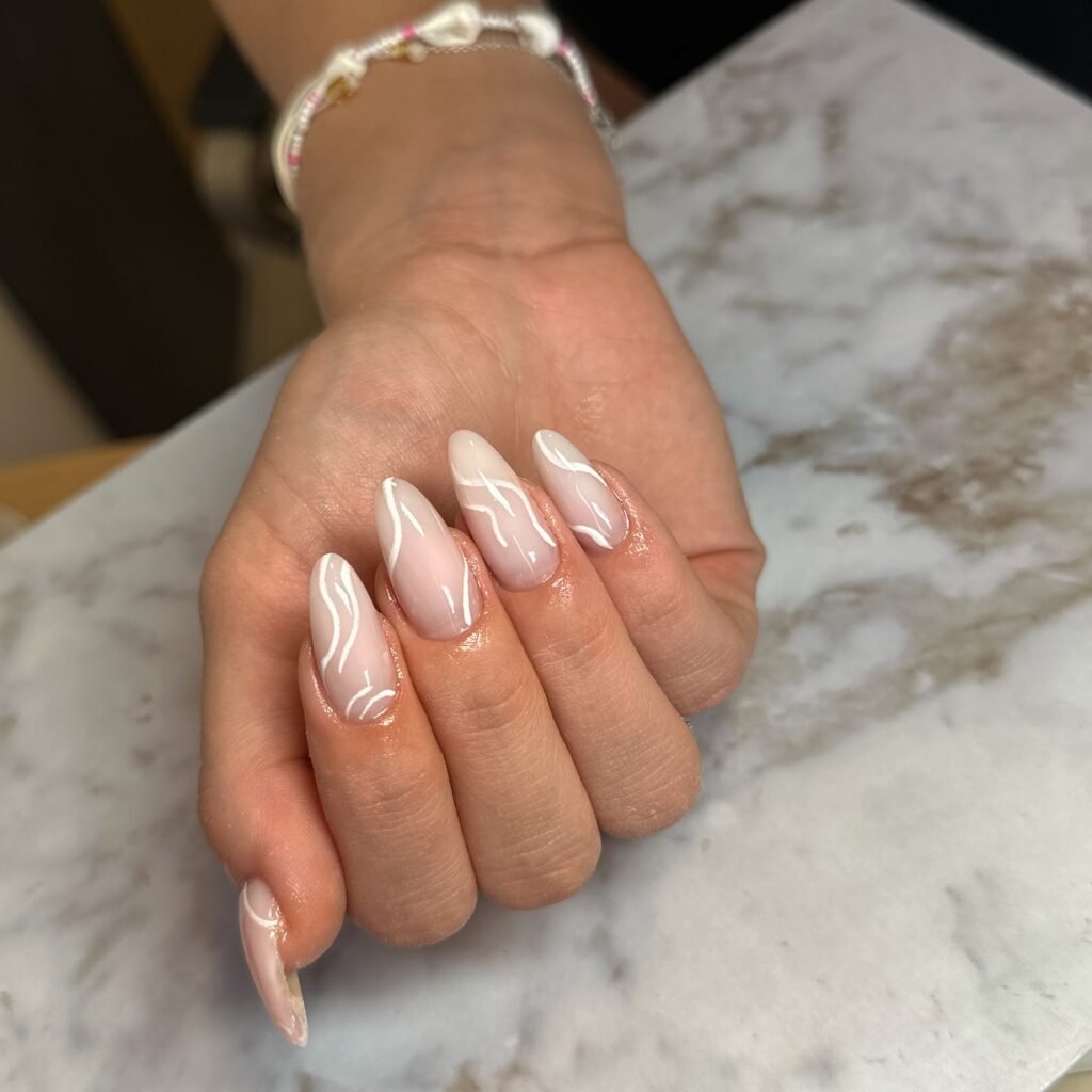 Stylish nails with white swirl design on a marble surface, showcasing glossy, well-manicured hands.