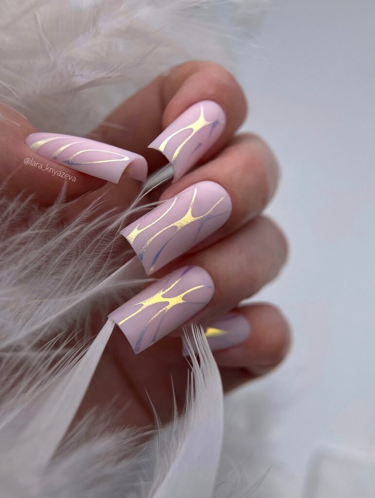 Chic pink nails with gold and white swirl design, softly holding white feathers for an elegant look.