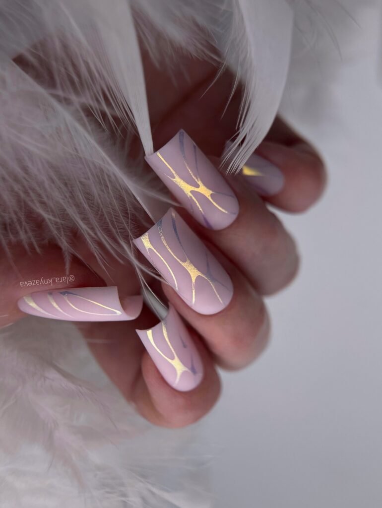 Elegant pink nails with gold accents surrounded by soft white feathers.