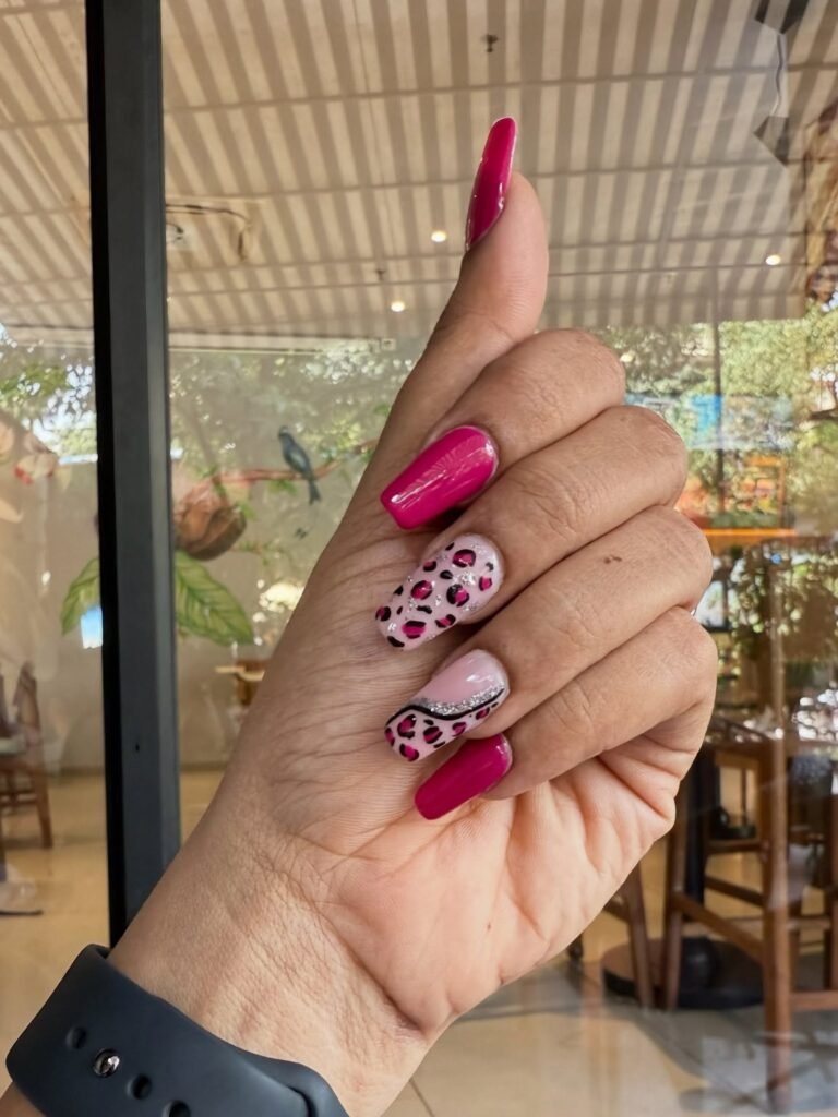 Hand with pink and leopard print nail art, displaying intricate designs in cafe setting. Fashionable nail art inspiration.