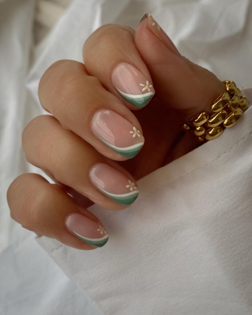 Elegant pastel French manicure with floral accents on nails, styled with gold rings and a white shirt.