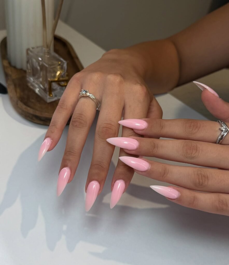 Close-up of hands with shiny pink stiletto nail art, adorned with silver rings.