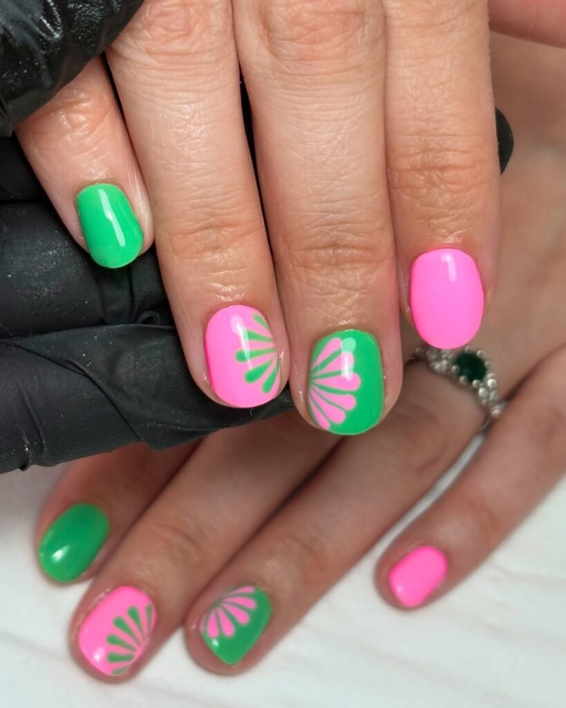 Bright pink and green nail art with floral designs on polished fingertips, showcasing trendy, vibrant manicure styles.