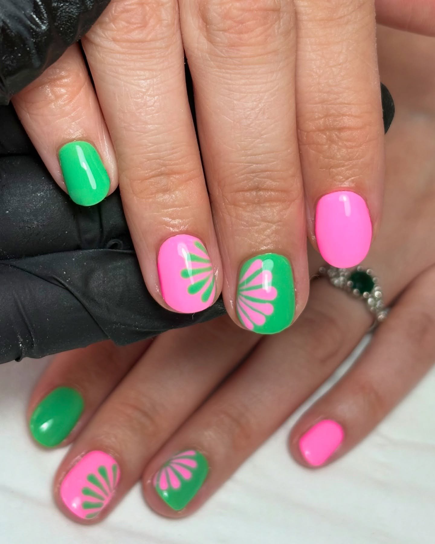 Bright pink and green nail art with floral designs on polished fingertips, showcasing trendy, vibrant manicure styles.