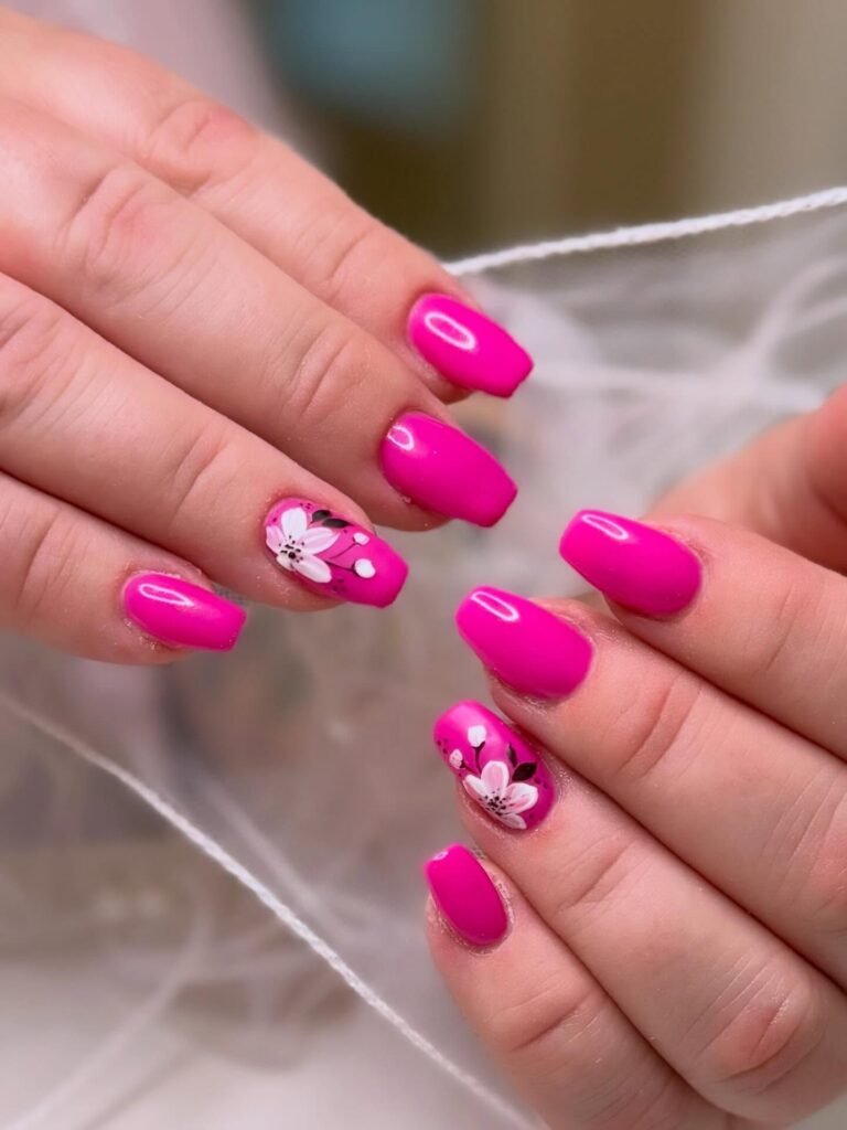 Bright pink nails with white floral designs, perfect for a stylish manicure.