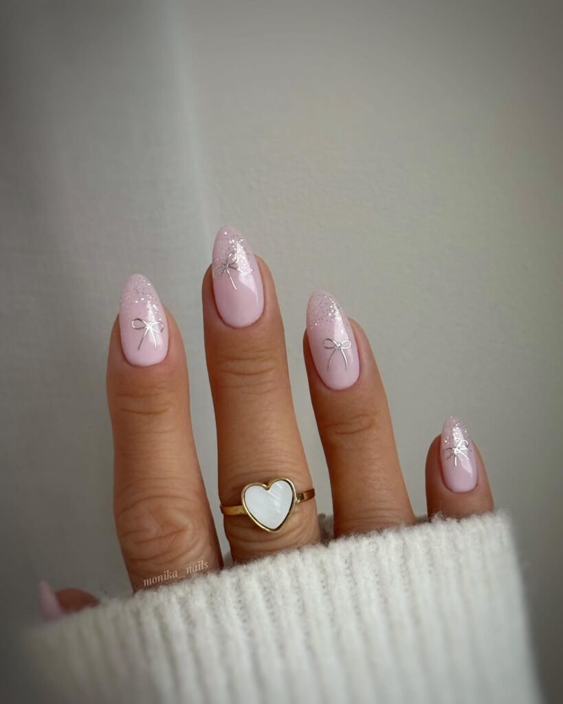 Pastel pink nails with delicate silver bow designs, heart ring on finger. Cozy, elegant manicure aesthetic.