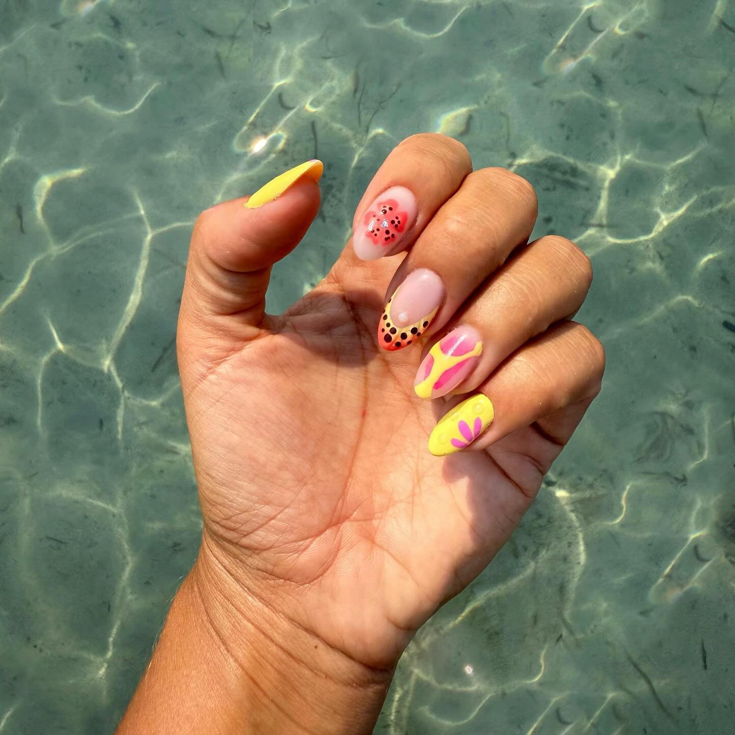 Bright summer nail art with floral and abstract designs on hand over clear water background.