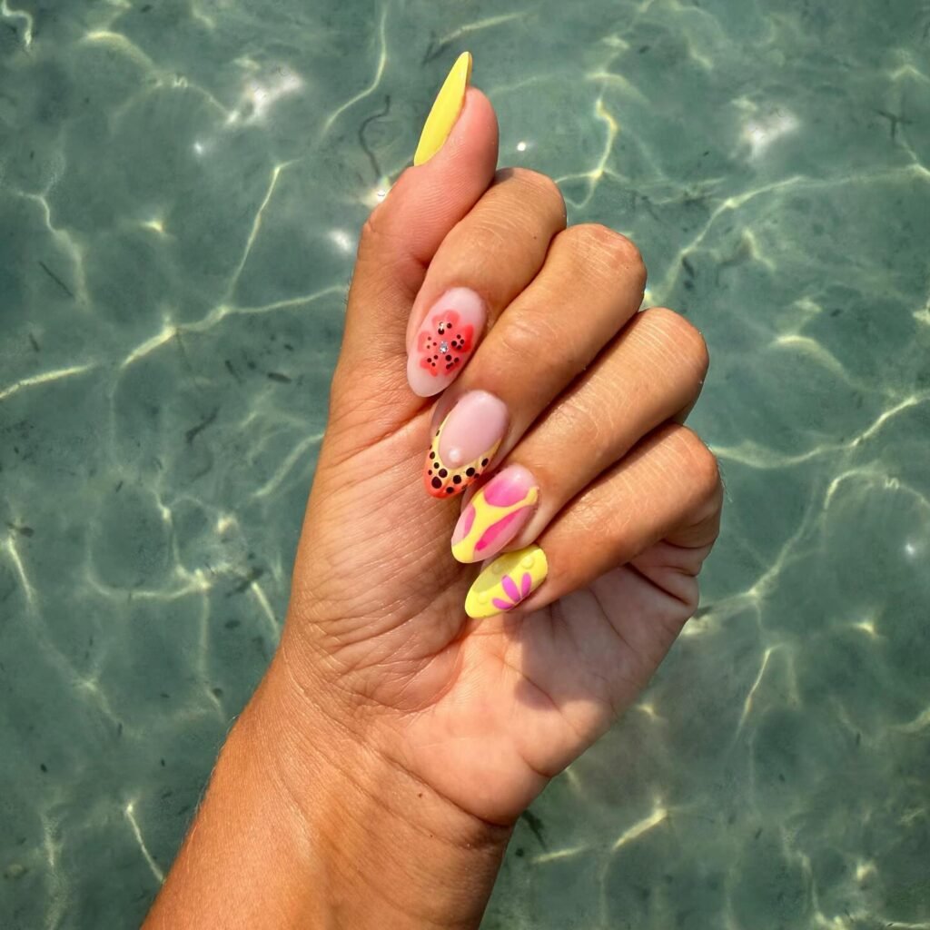 Vibrant floral nail art with pink and yellow designs on a hand over clear water background. Perfect summer manicure.