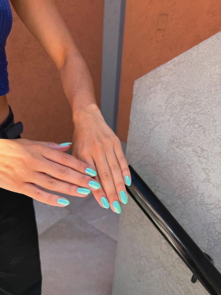 Person displaying hands with vibrant turquoise nail polish against a textured background.