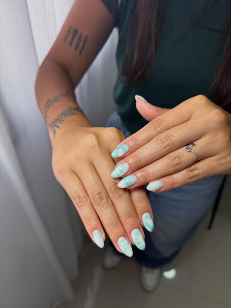 Close-up of hands with green and white abstract nail art, showcasing stylish manicure and arm tattoos.