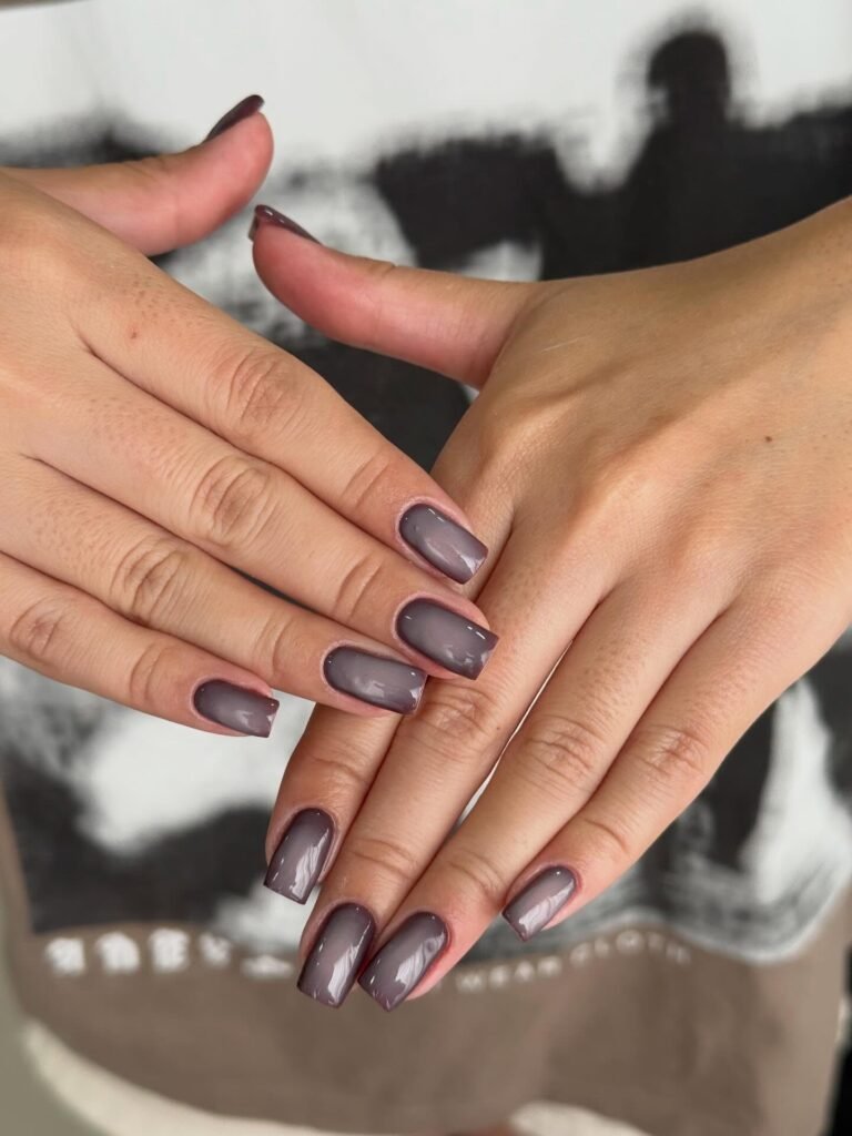 Close-up of hands with glossy grey nail polish, showcasing elegant manicure design.