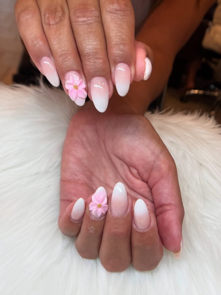 Pink ombre nails with 3D floral design on a fluffy white background. Fashionable manicure inspiration.