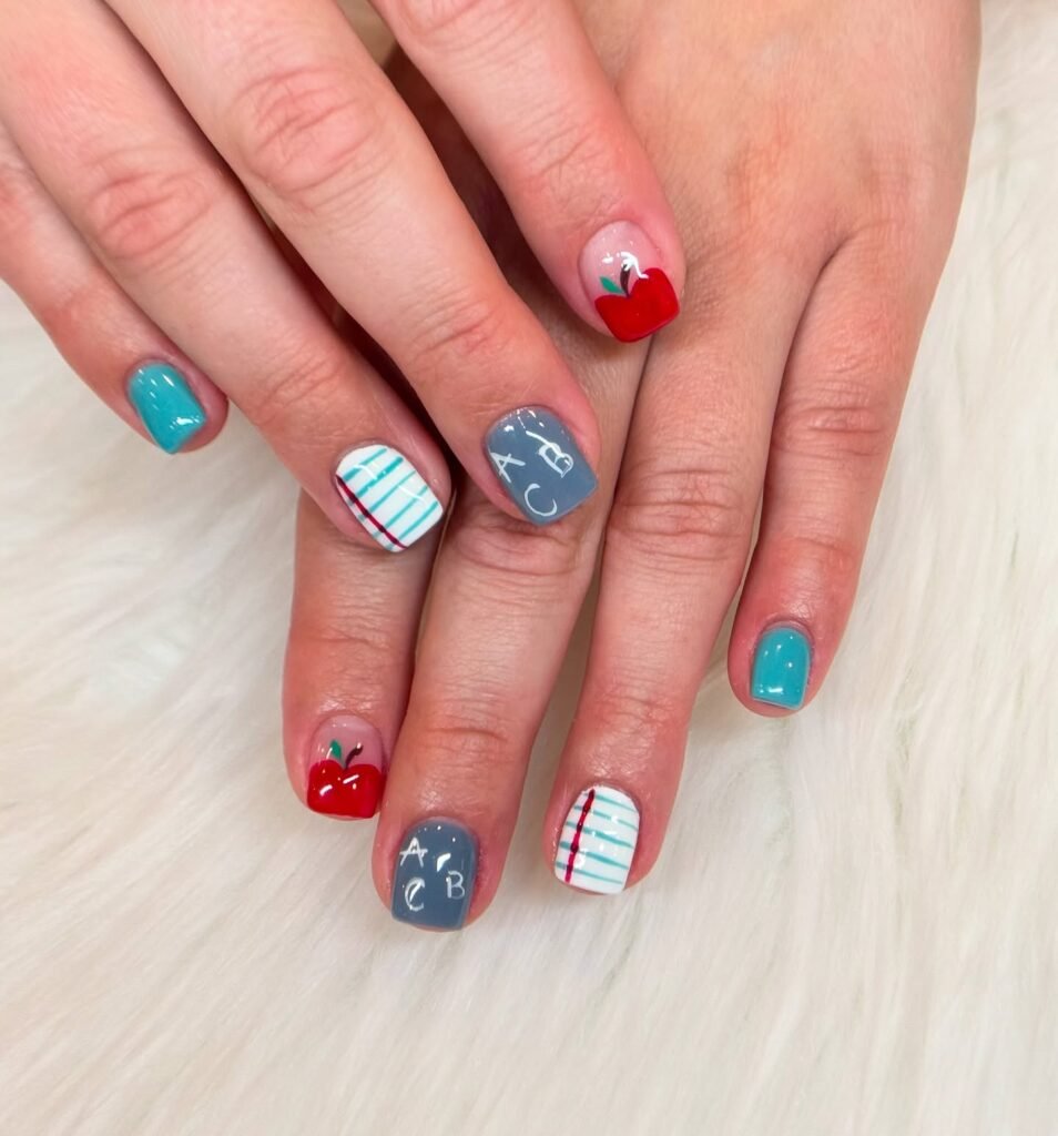 Colorful back-to-school nail art featuring apples, lined paper, and ABC letters on a white background.
