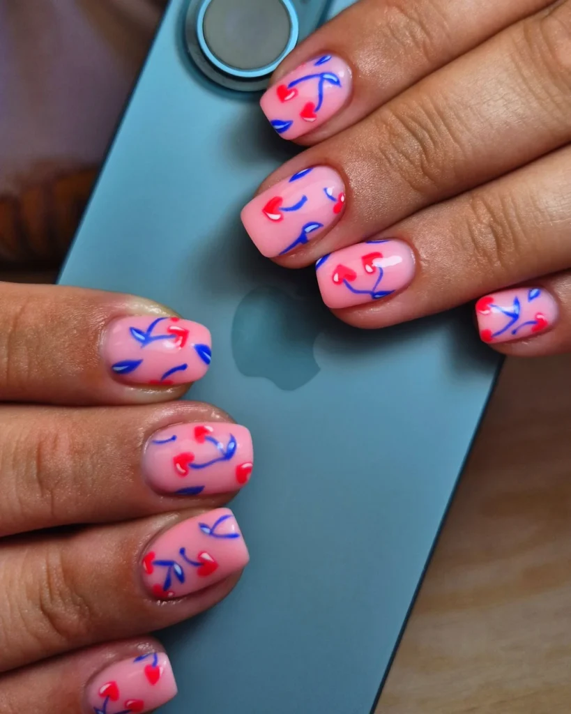 Colorful nail art with red and blue designs on pink nails, holding a blue smartphone.